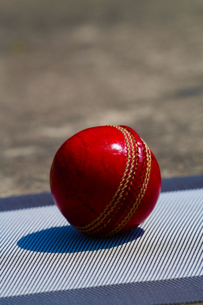 Vibrant red cricket ball on striped pitch surface in bright outdoor setting. Ideal for sports themes.