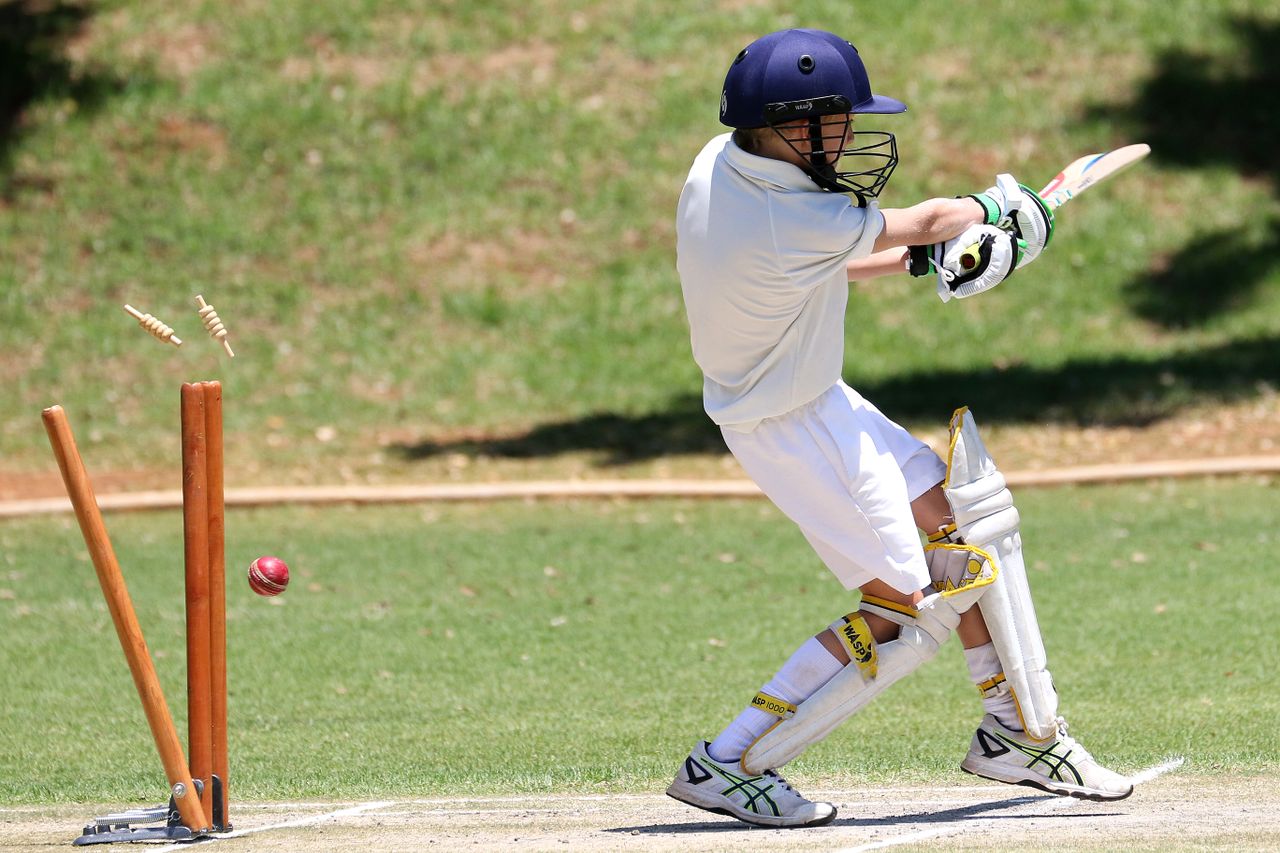 services-04 Young cricket player in full gear performing a sweep shot on a sunny day outdoors.