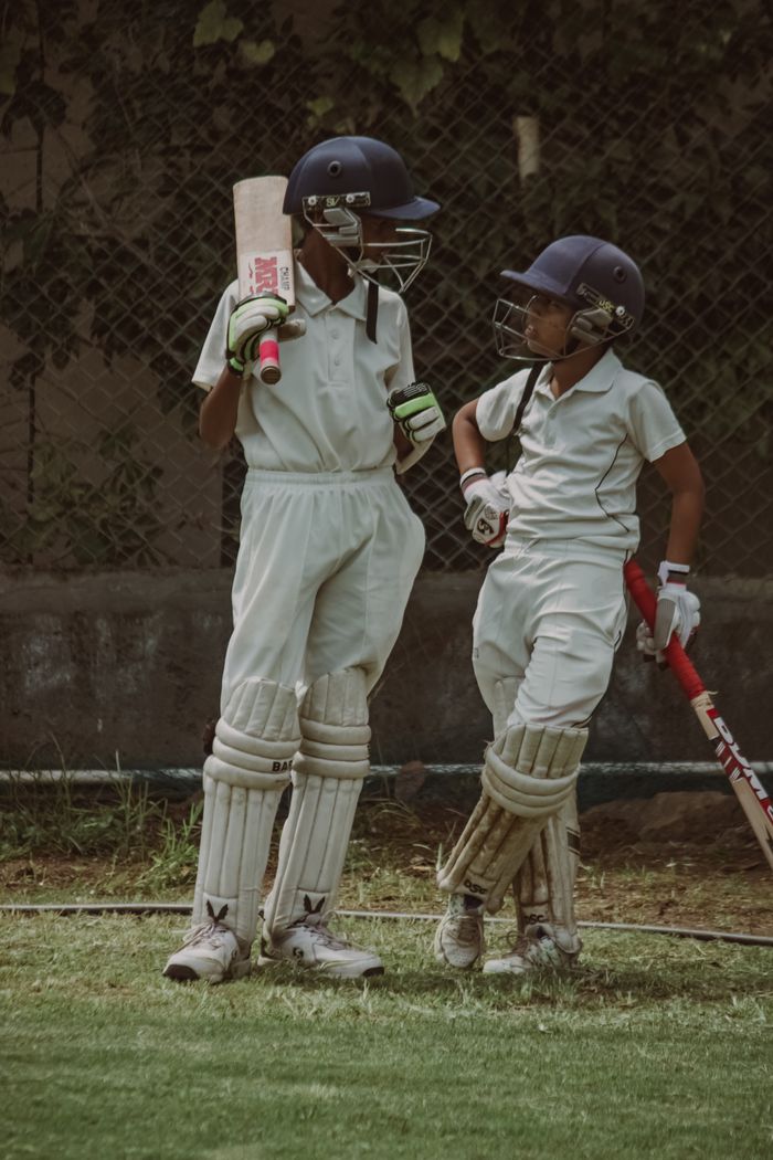 ours-journey Two young cricketers in full gear discussing strategy on the field in Gahunje, India.