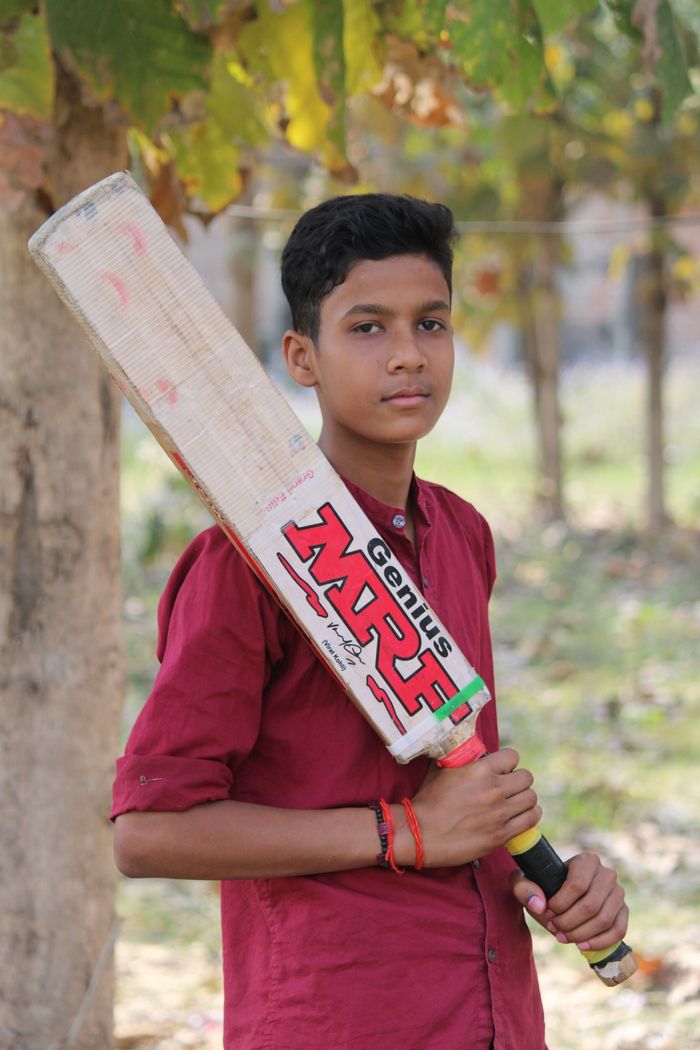 contact-img Teenager holding a cricket bat in a sunny park, showcasing sporty confidence.