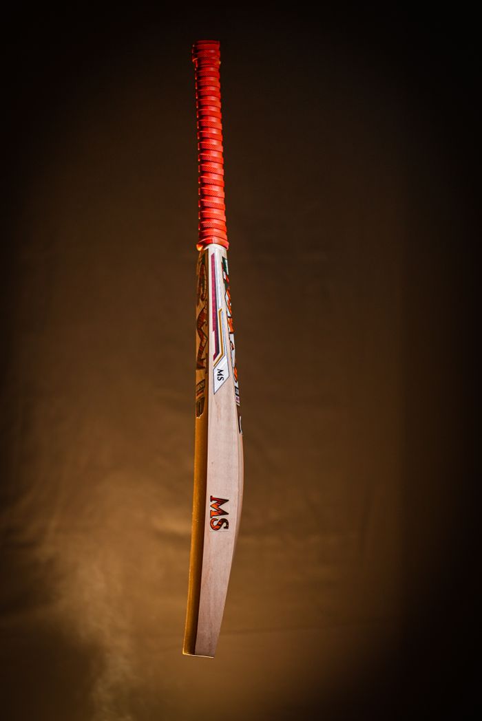 services-img Stylish cricket bat with red handle poised against a dark studio backdrop.