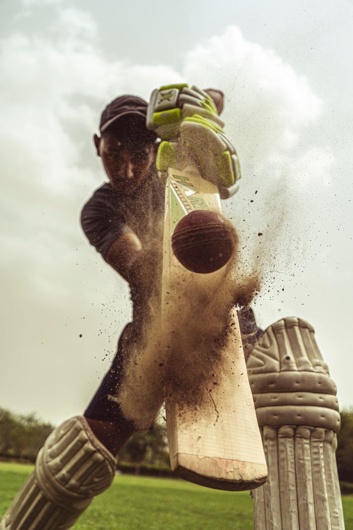 our-experience Cricketer in motion striking the ball with intense focus, clouds of dust captured.