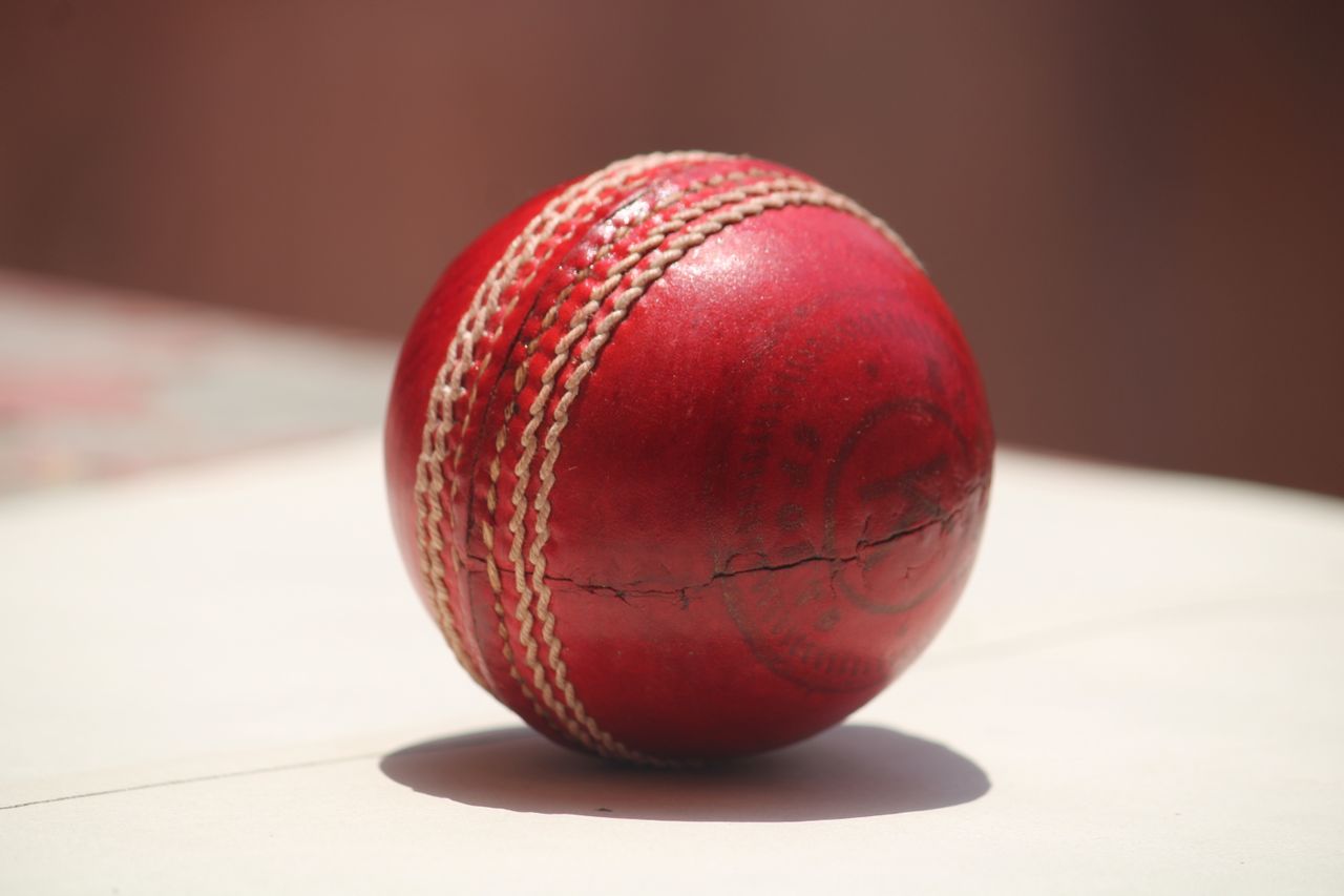 services-02 Detailed close-up of a red leather cricket ball showing wear and stitching.